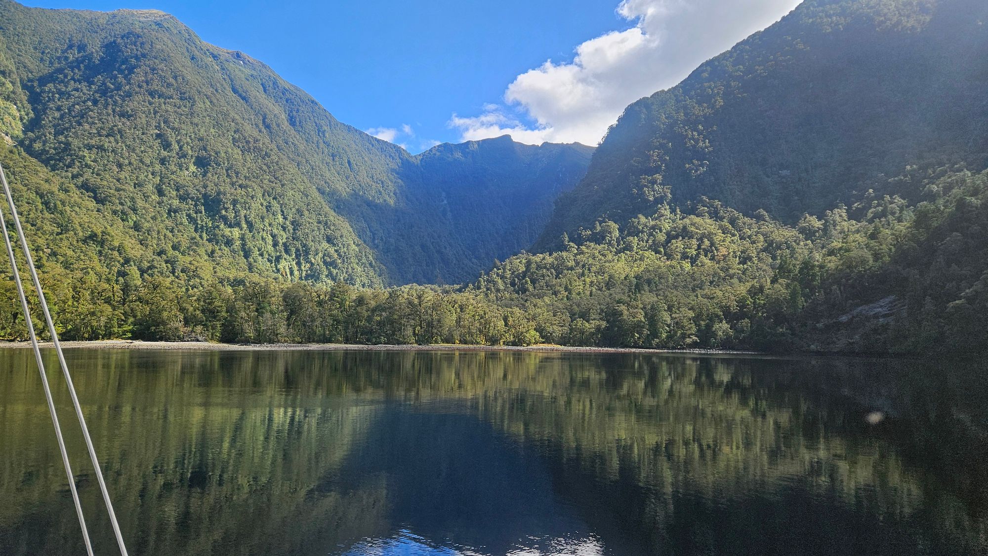 Matariki III at anchor in Dusky Sound, rigging in foreground, sun-drenched valley walls behind