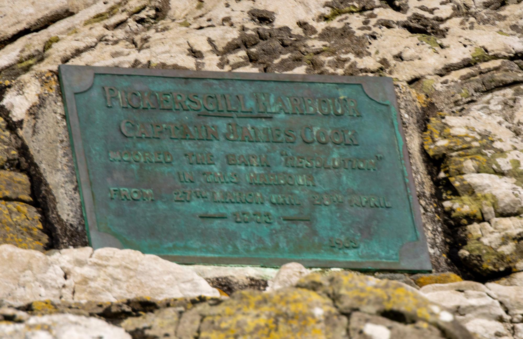 Weathered bronze plaque set into rock at Pickersgill Harbour reading: Captain James Cook moored the Bark Resolution in this harbour from 27th March to 28th April 1773