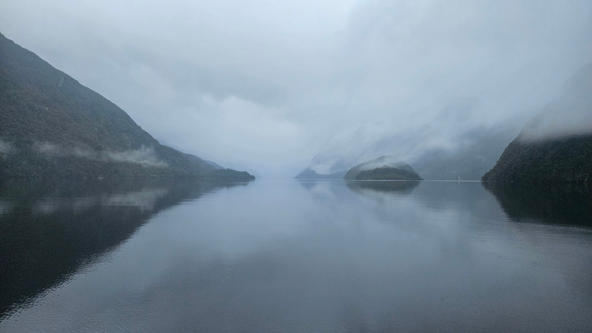 Perfect mirror reflection of misty mountains in the glassy water of Dusky Sound at dawn