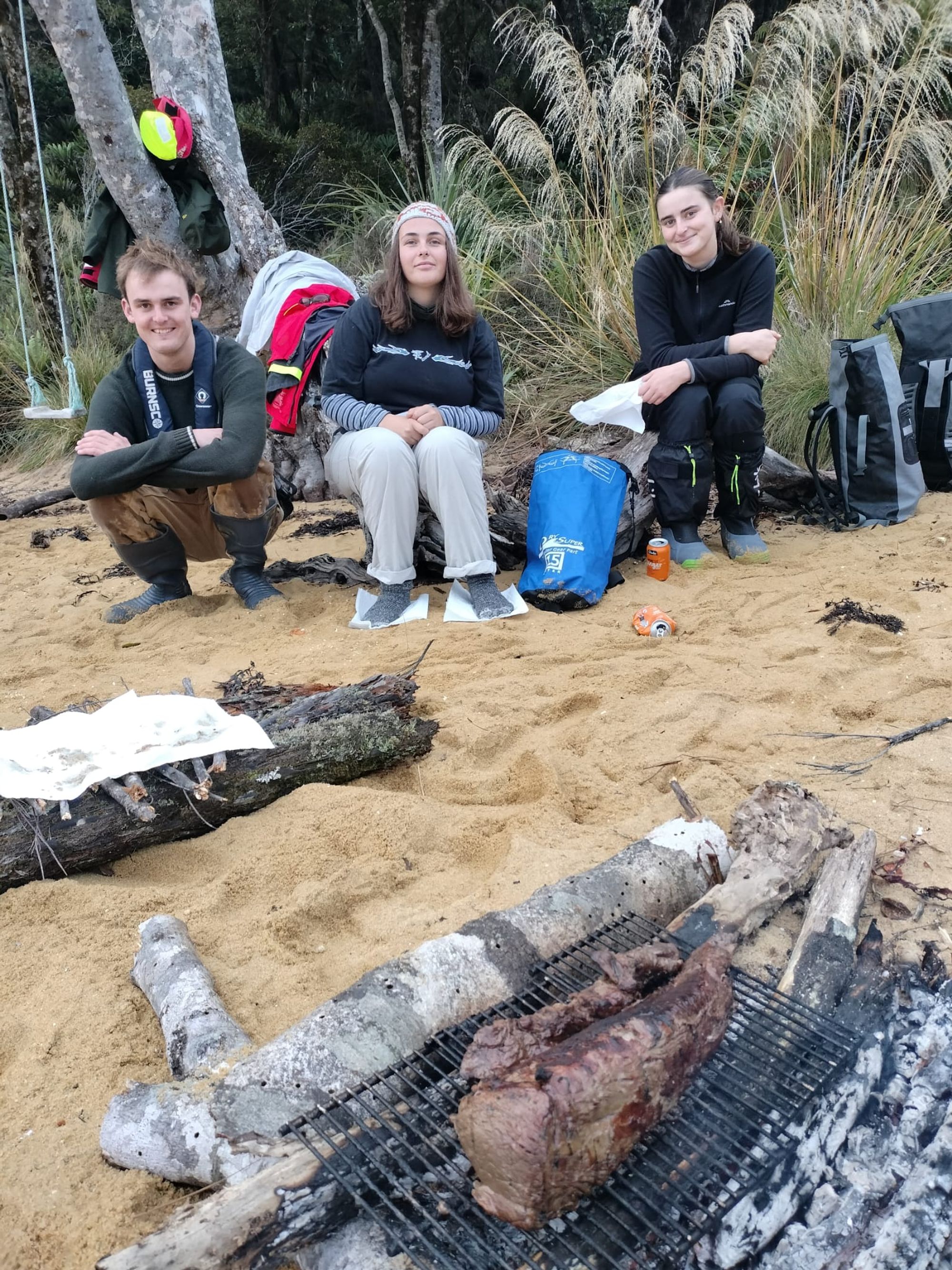 The crew gathered around the driftwood fire at Abraham's Bosom beach BBQ, Stewart Island