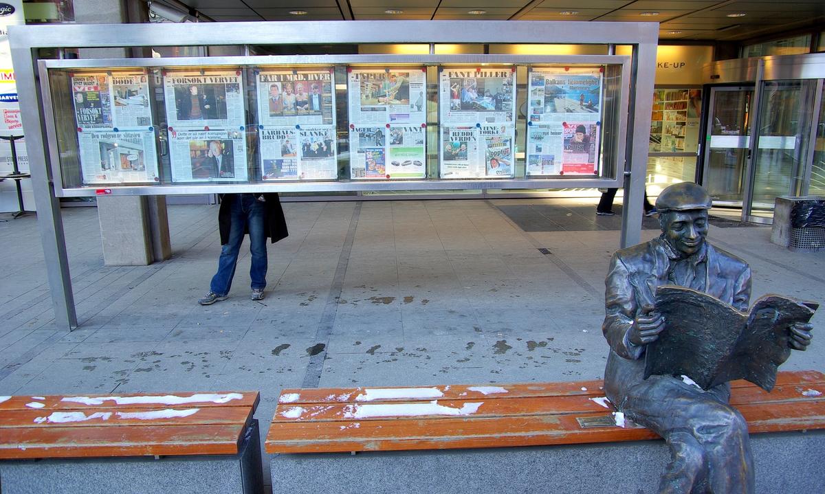 Photo d'une statue d'un homme lisant un journal, devant des unes du journal VG