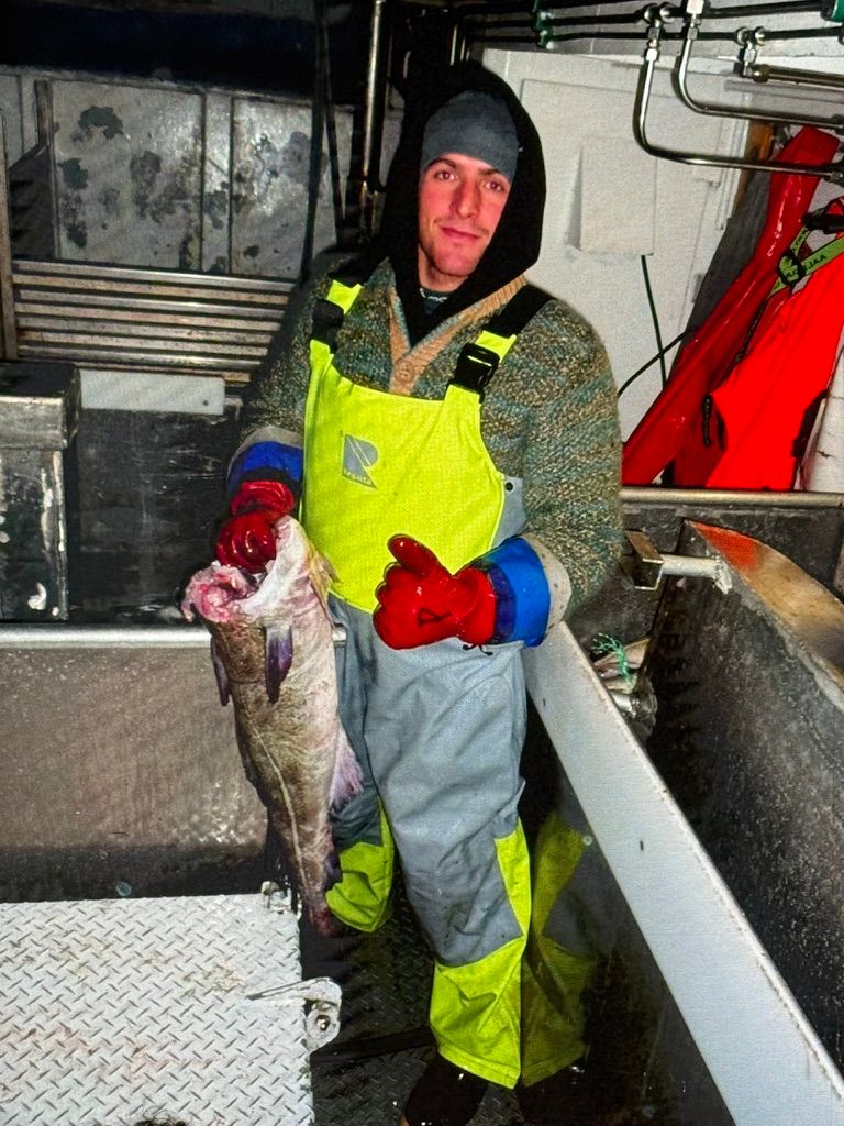 Vincent tenant un poisson dans la main sur un bateau de pêche, de nuit