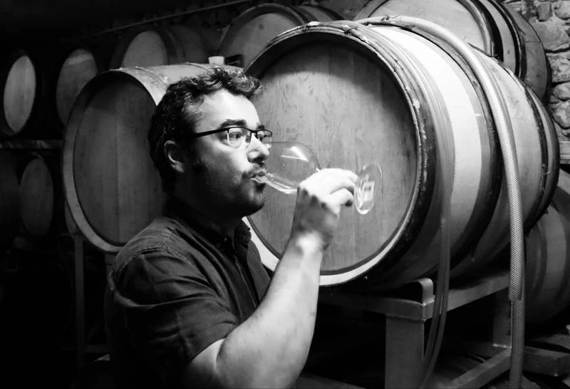 Lionel buvant un verre de vin devant un tonneau