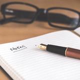 Cahier ouvert avec marqué "Notes". Stylo sur le cahier. Paire de lunettes en arrière plan.
