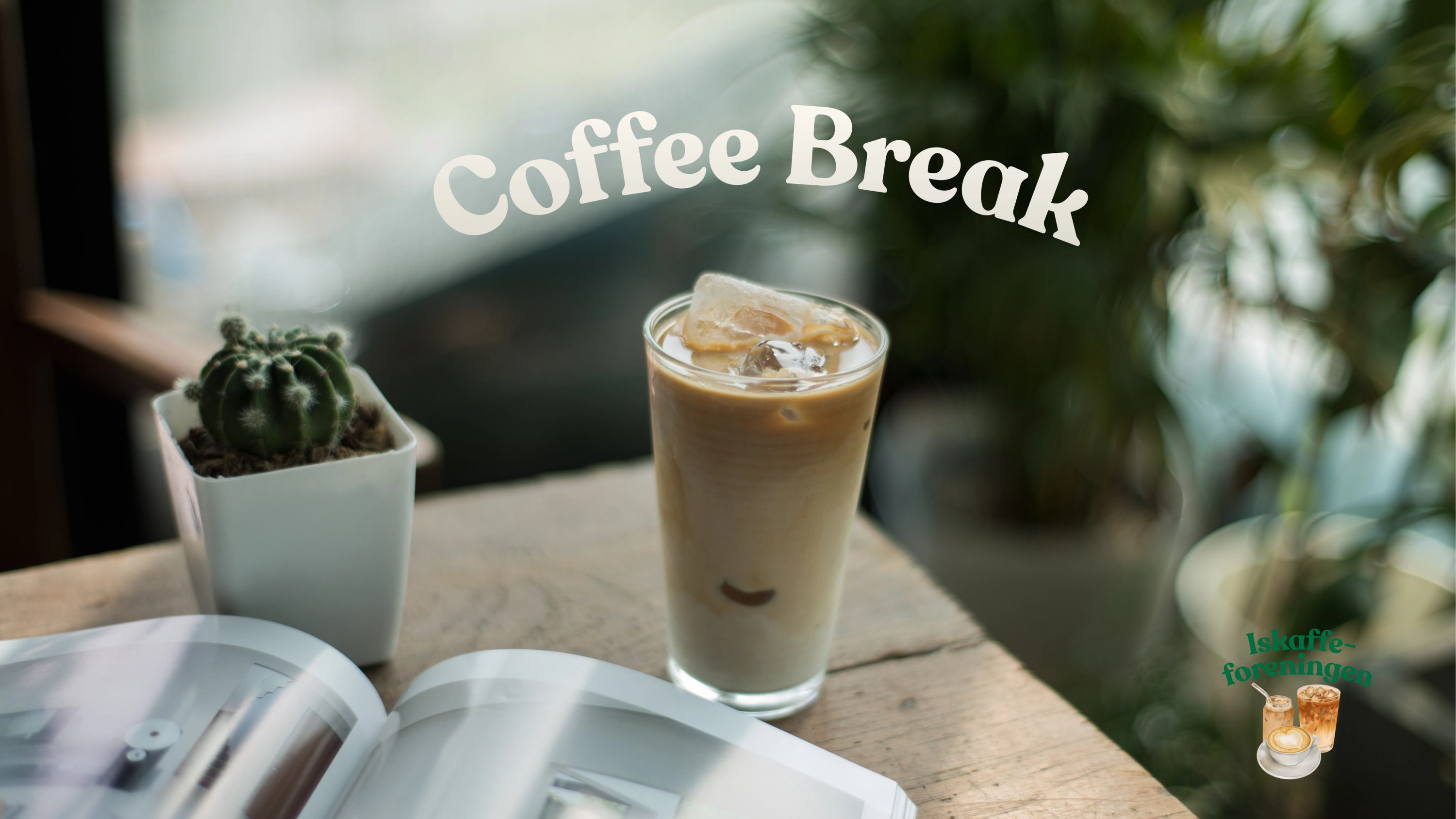 Et glass iskaffe med isbiter står på et trebord ved siden av en liten kaktus i hvit potte og et oppslått magasin, med teksten «Coffee Break» skrevet over i bakgrunnen.