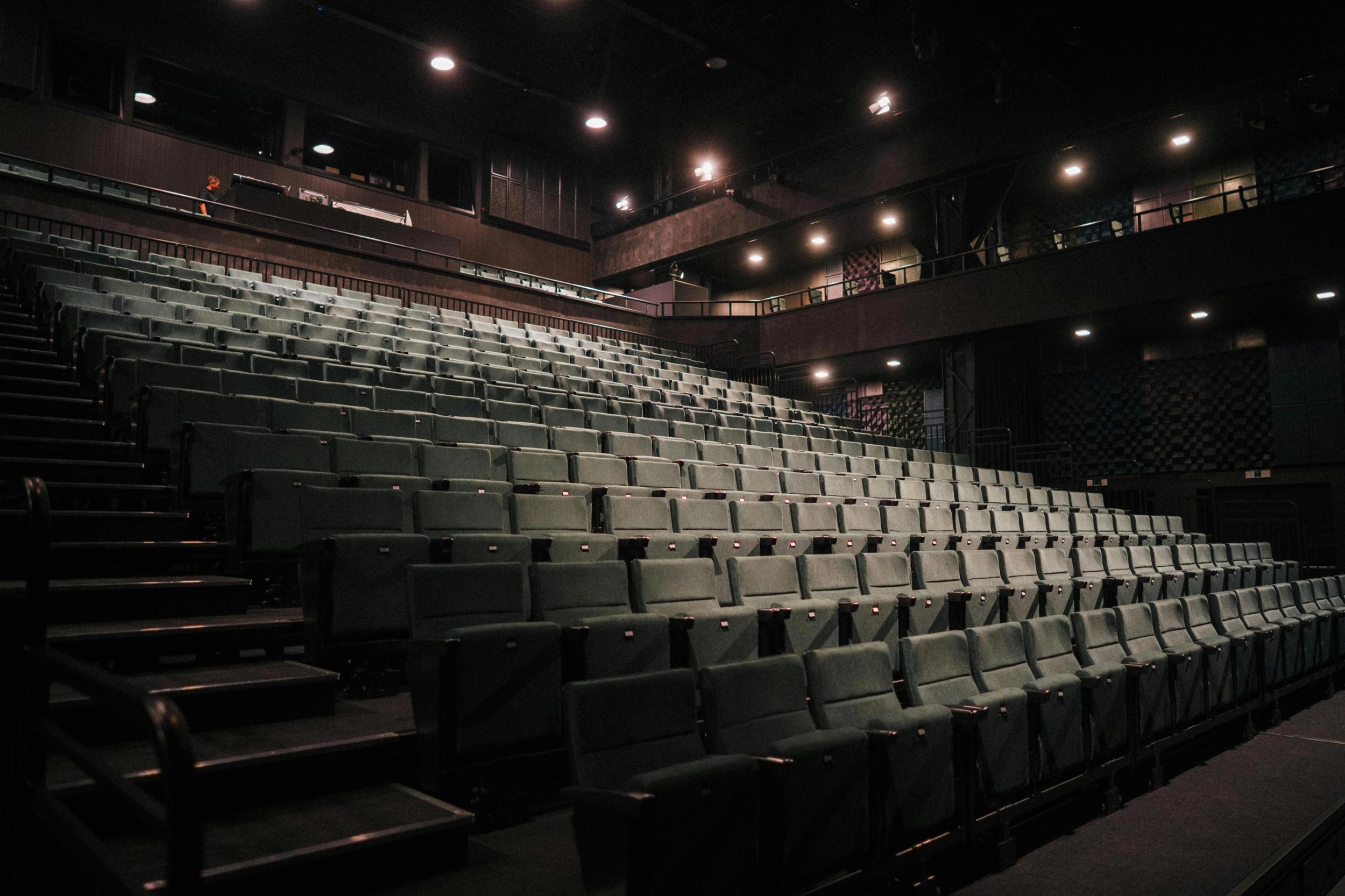 Tomt amfi med rekker av grønne seter i en mørklagt teatersal, opplyst av svake taklys.