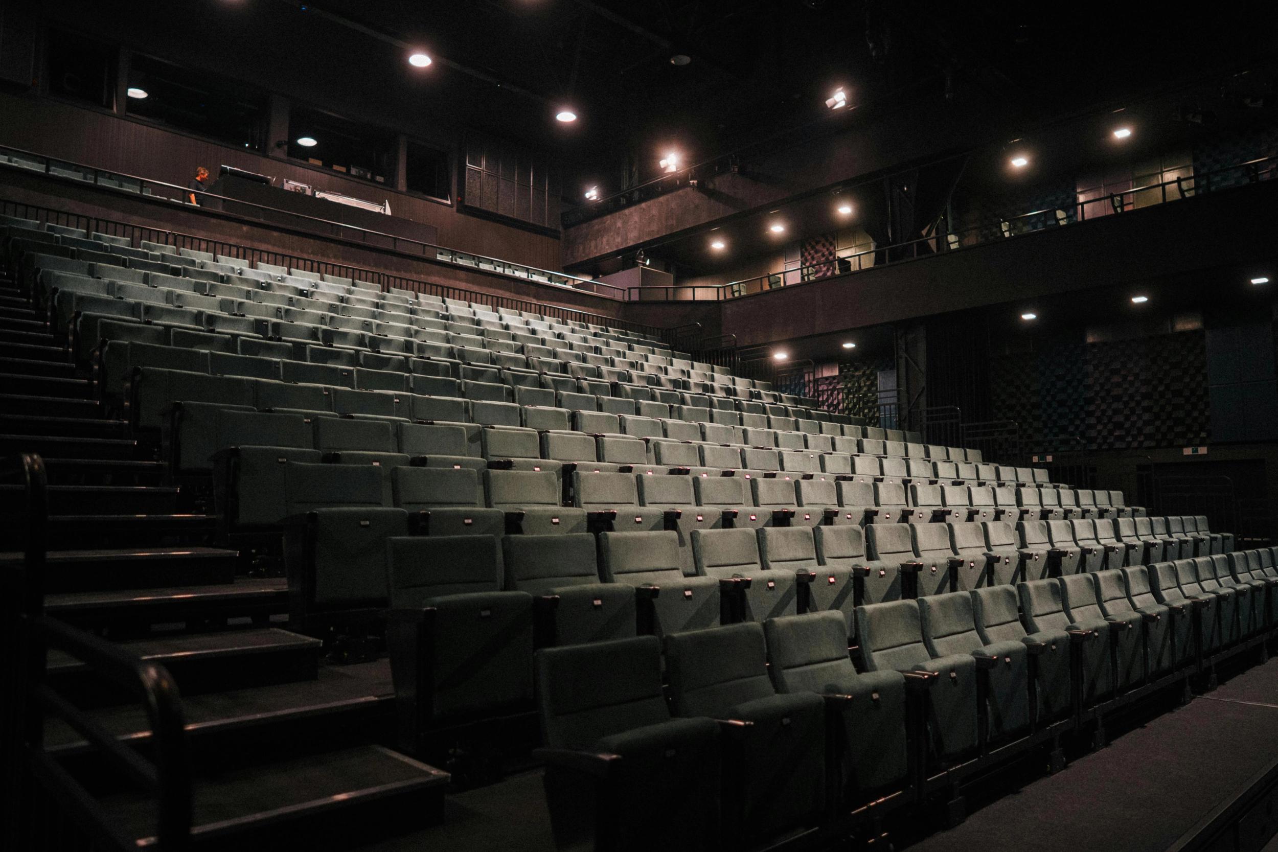 Tomt amfi med rekker av grønne seter i en mørklagt teatersal, opplyst av svake taklys.
