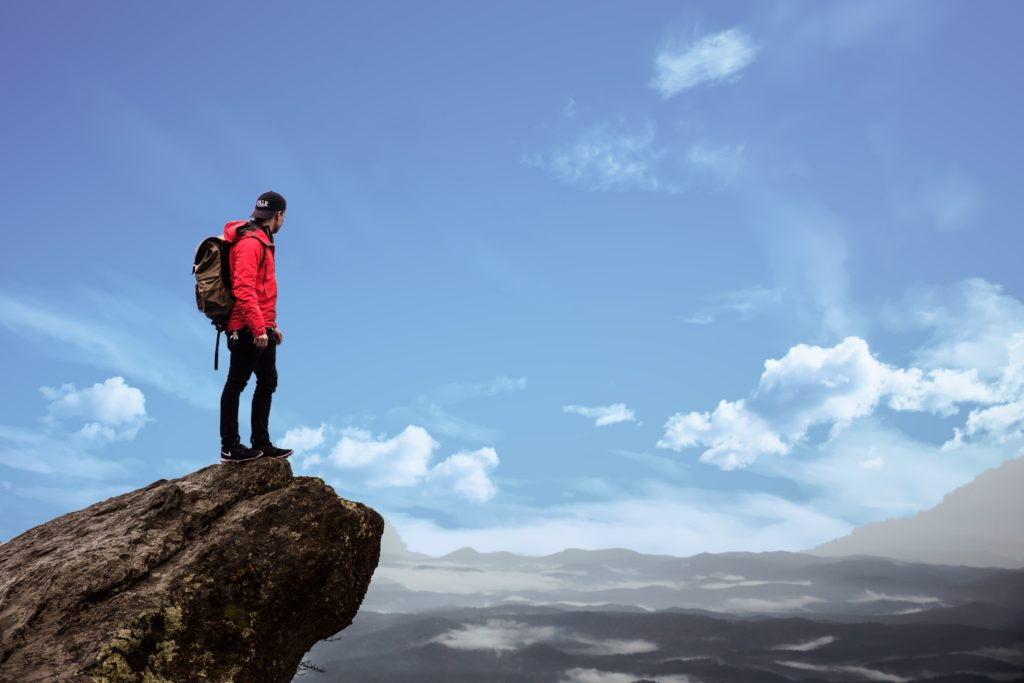 Hiker standing on a rocky cliff overlooking a wide mountain landscape.