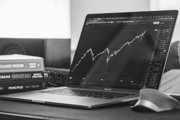 Black-and-white laptop showing a rising stock chart beside finance books.