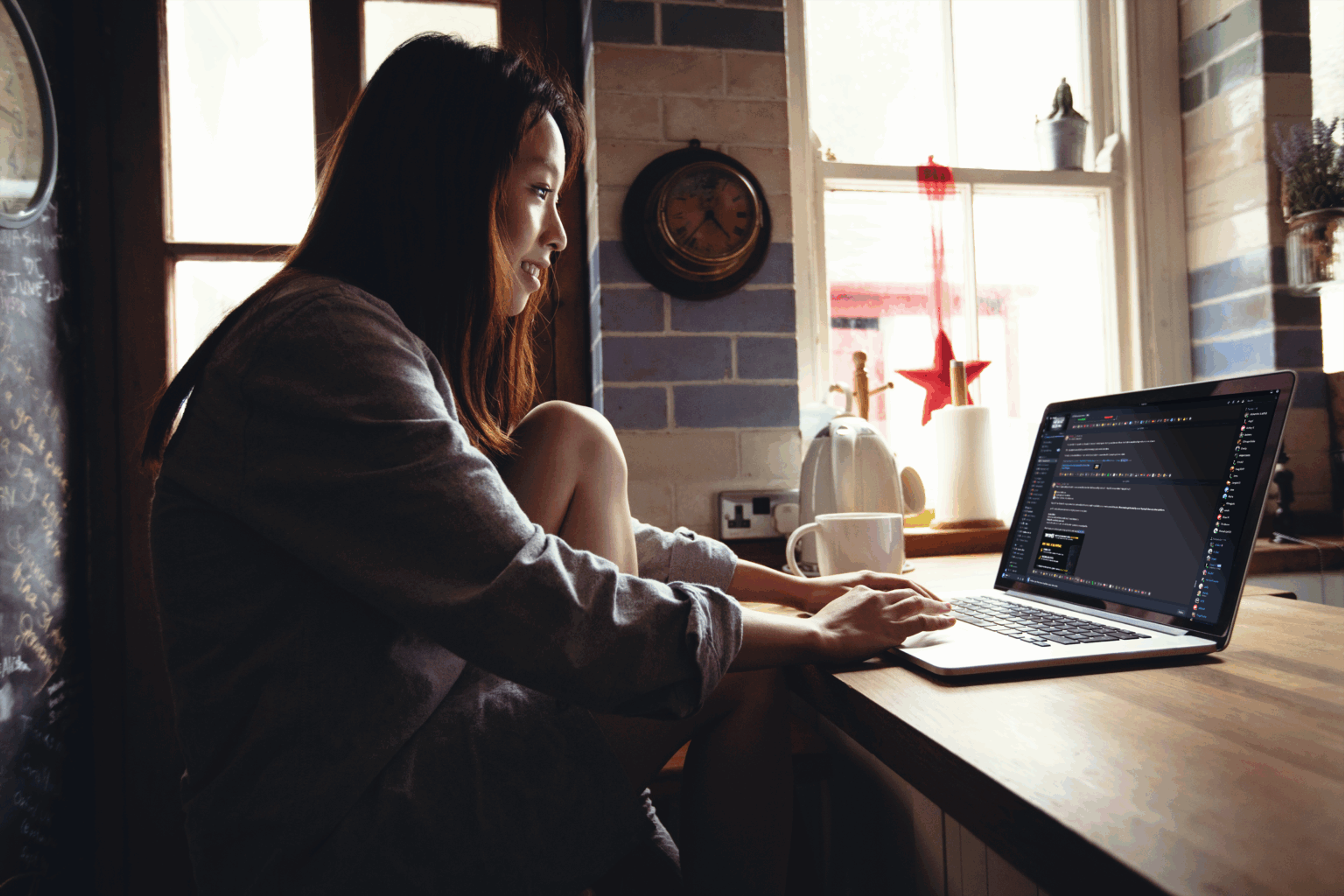 Person working on a laptop at a kitchen table in a softly lit home setting