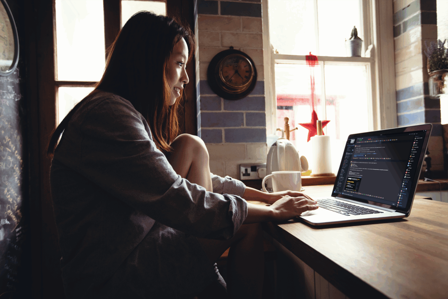 Person working on a laptop at a kitchen table in a softly lit home setting