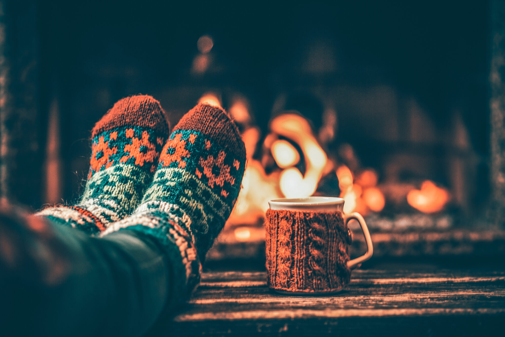 Cozy socks and hot drink by fireplace creating warm winter mood