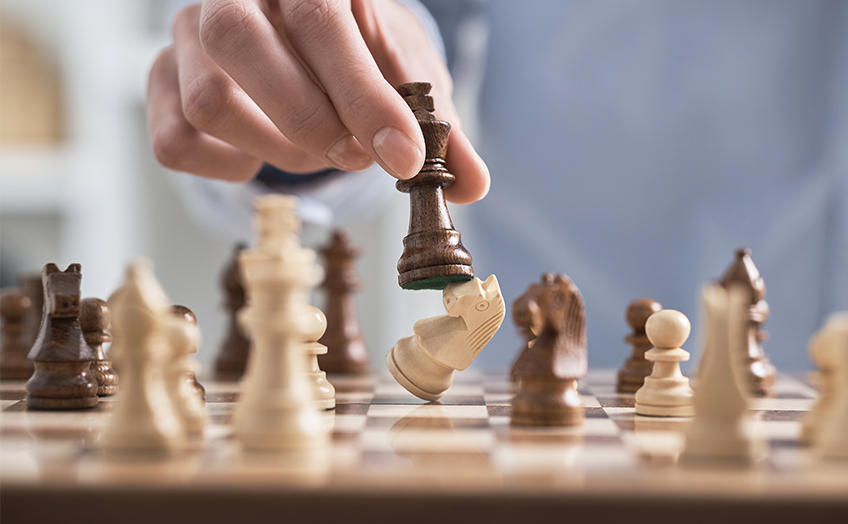 Hand moving a chess piece to capture an opponent’s piece on a chessboard.