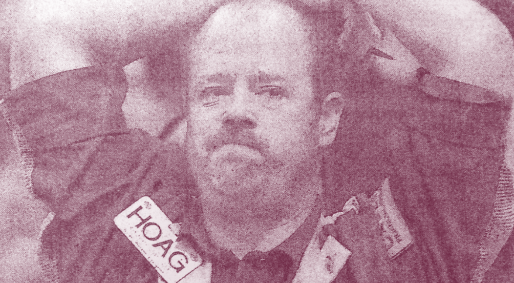 Grainy photo of a man in a jacket with a visible HOAG badge in a muted sepia tone.