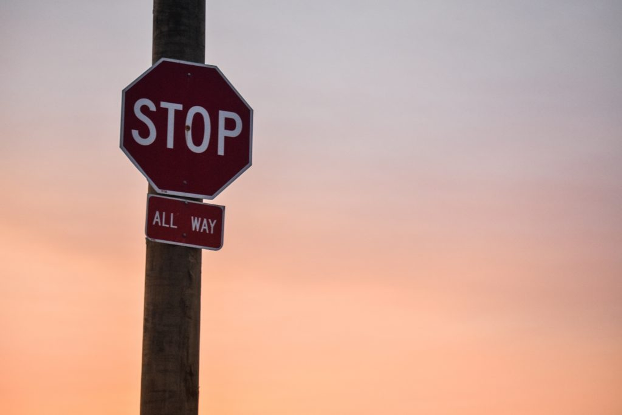 Stop sign on a pole against a soft sunset sky.