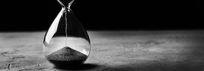 A black-and-white photo of sand falling through an hourglass on a textured surface.