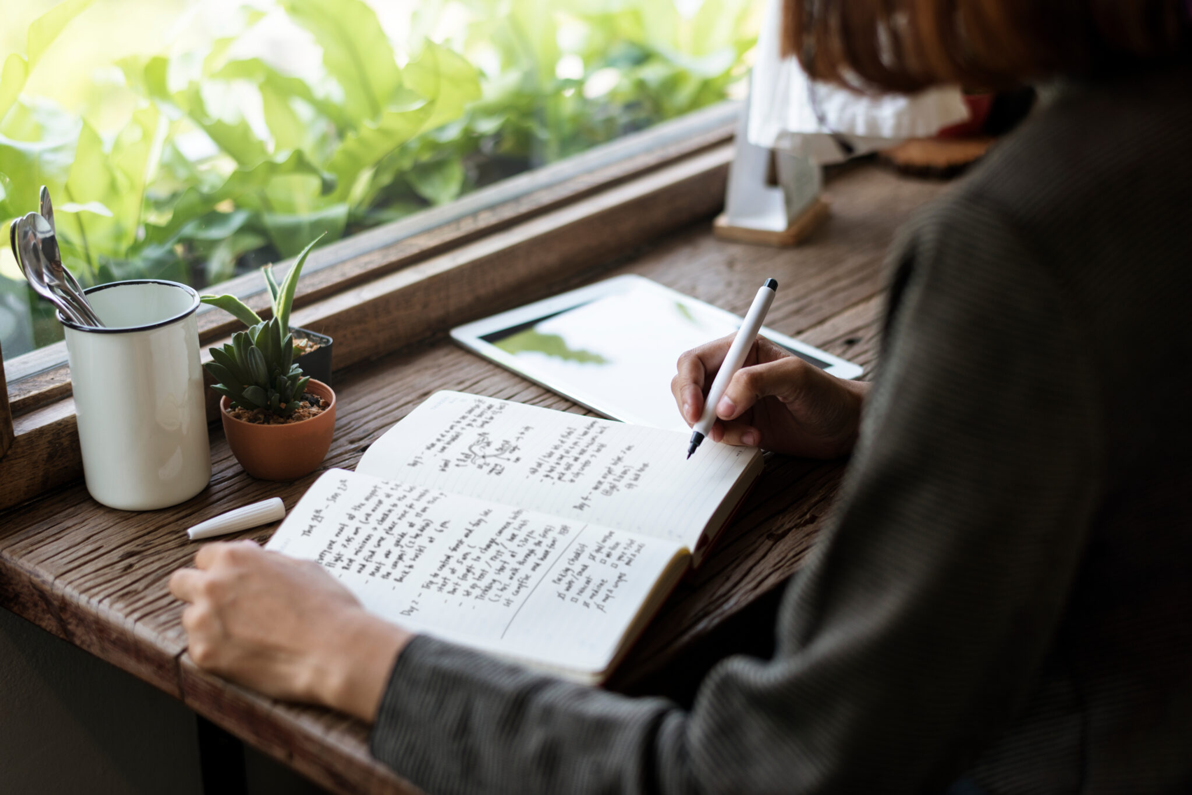 Woman sitting at a desk in front of her window writing into a journal