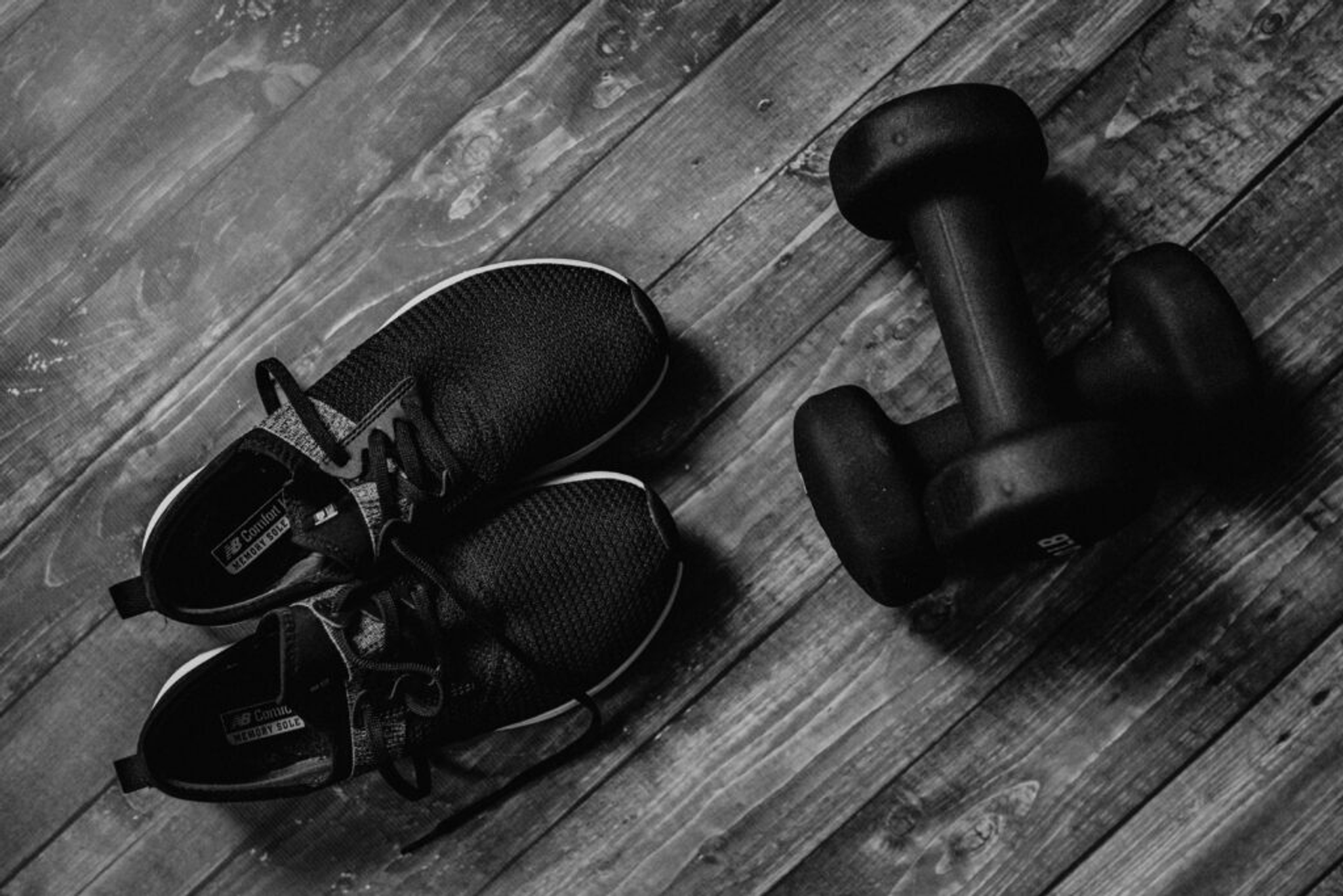 Running shoes and dumbbells on a wooden floor, symbolizing fitness training.