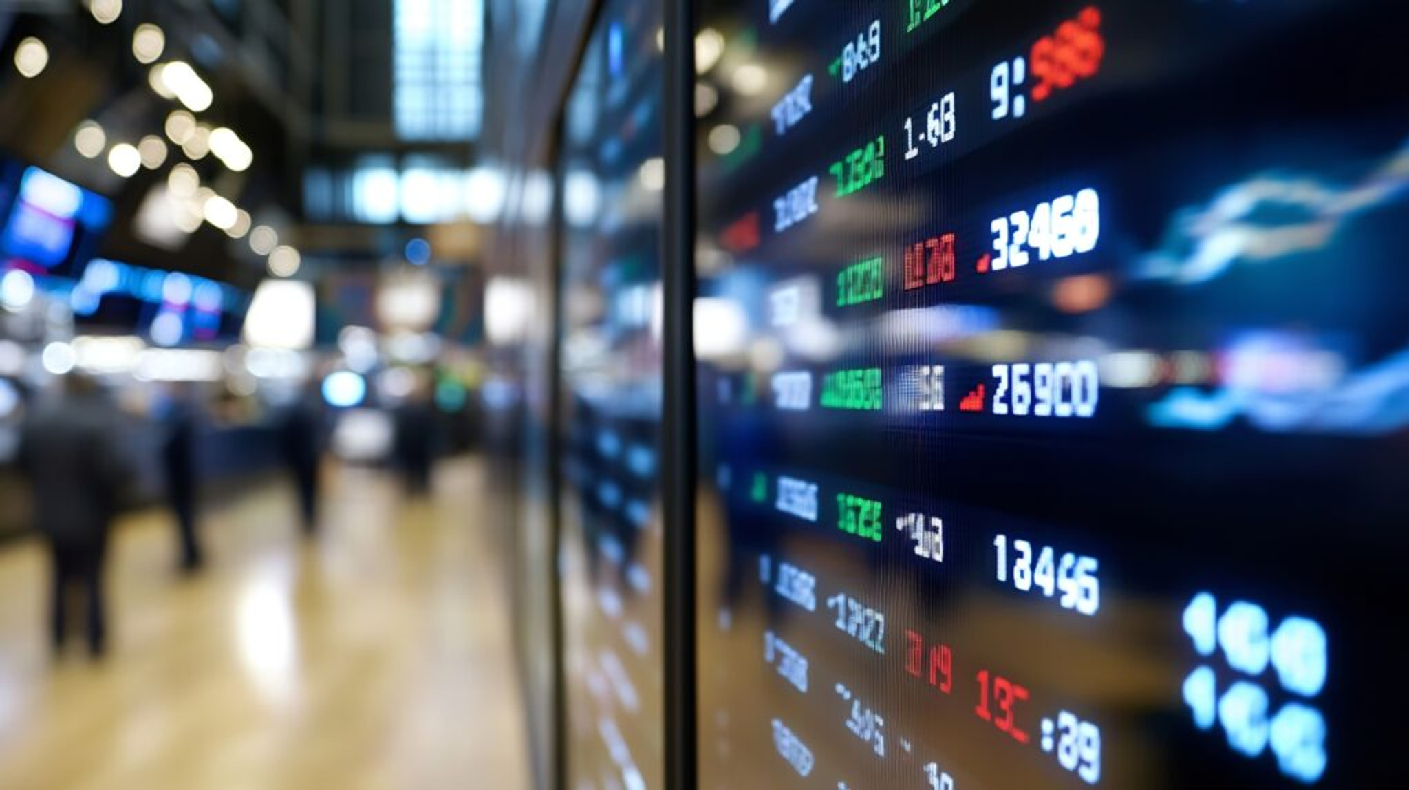 A side-angle view of a digital stock market display board inside a large financial building.
