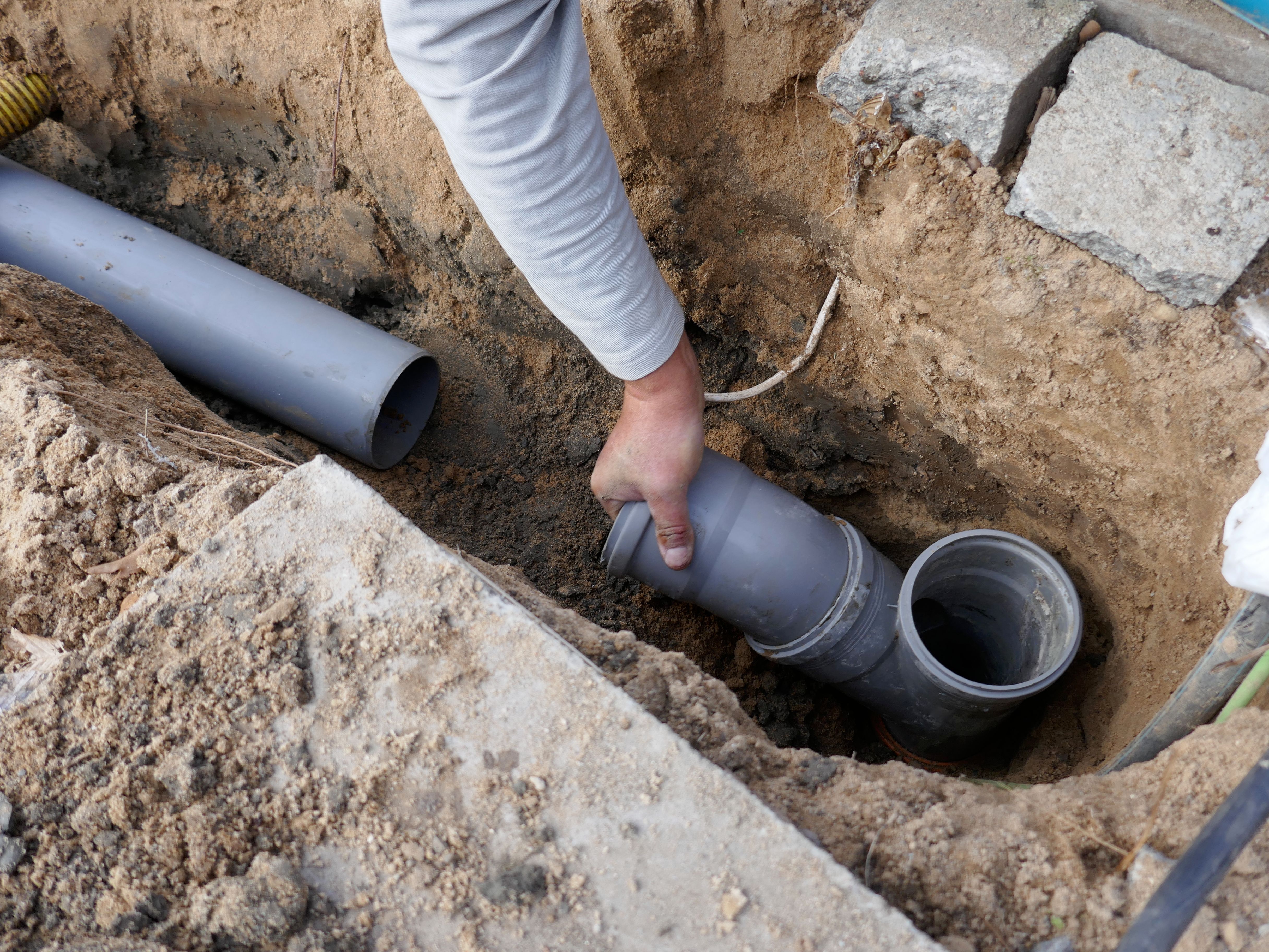Plumber installing underground drainage pipes in an excavated trench.