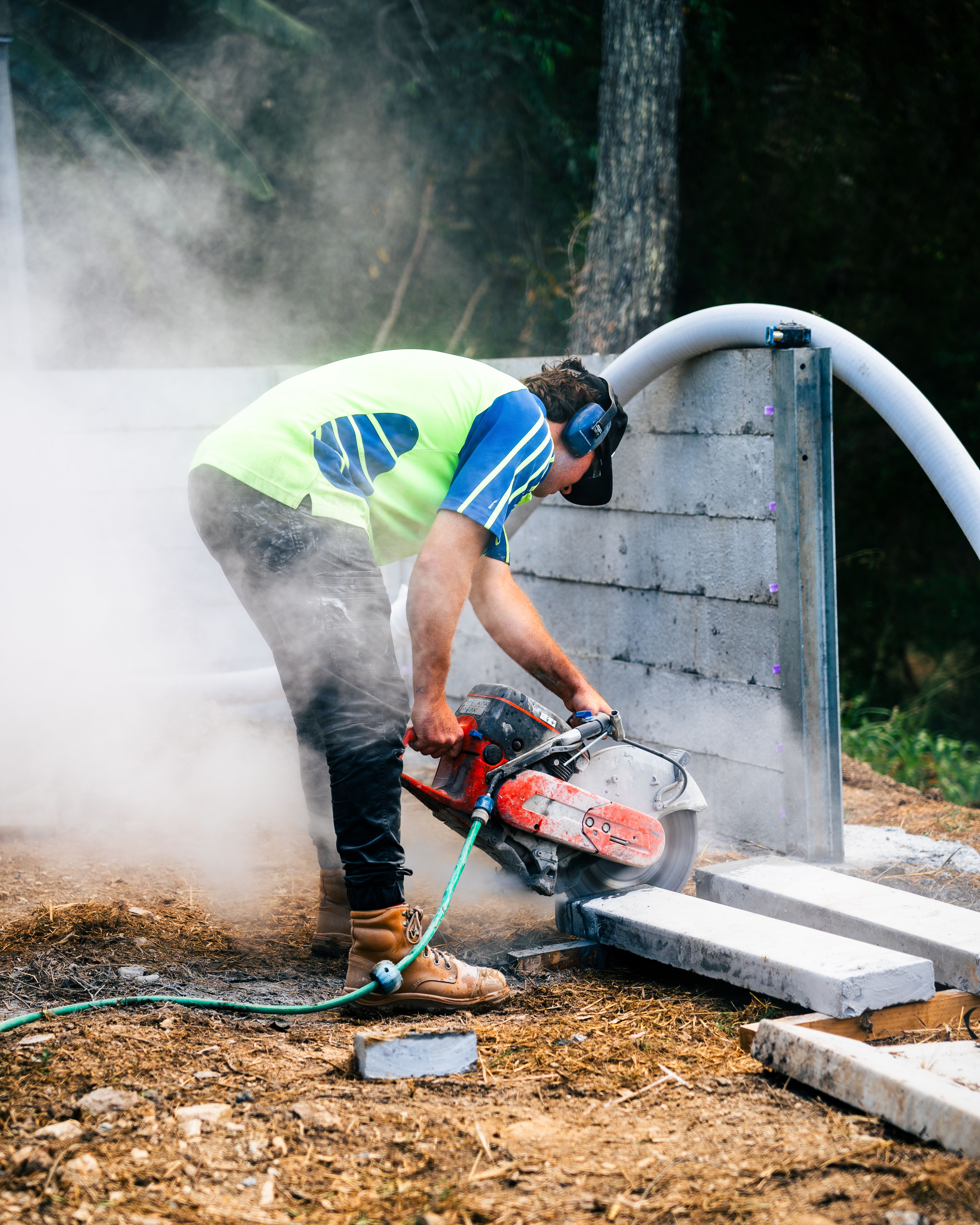Concreter cutting concrete blocks on a construction site with a wetsaw, wearing hi-vis vest and ear protection