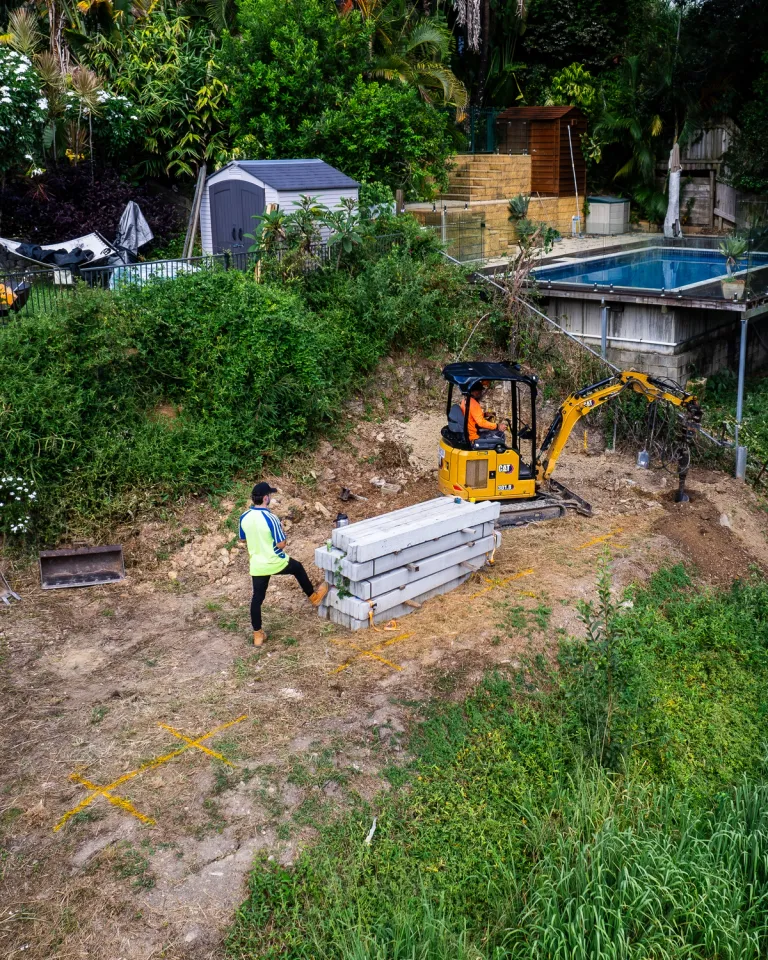 Landscapers using a mini excavator to prepare a residential backyard for retaining wall construction.