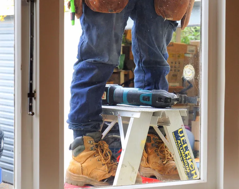 Handyman on a stepladder using an oscillating saw
