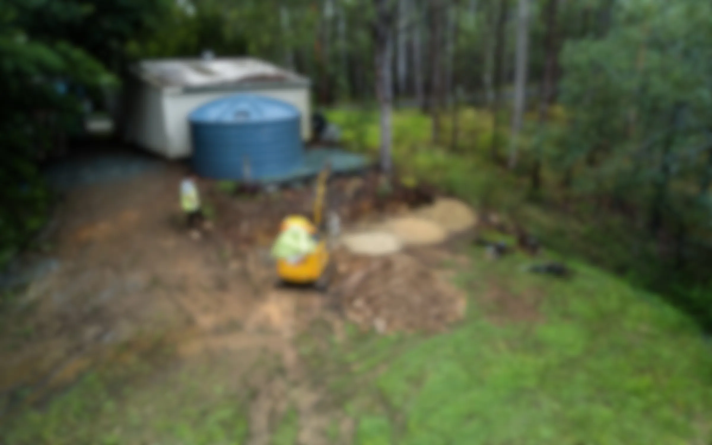 Landscapers using a mini excavator to prepare a sloped residential garden site in Australia.
