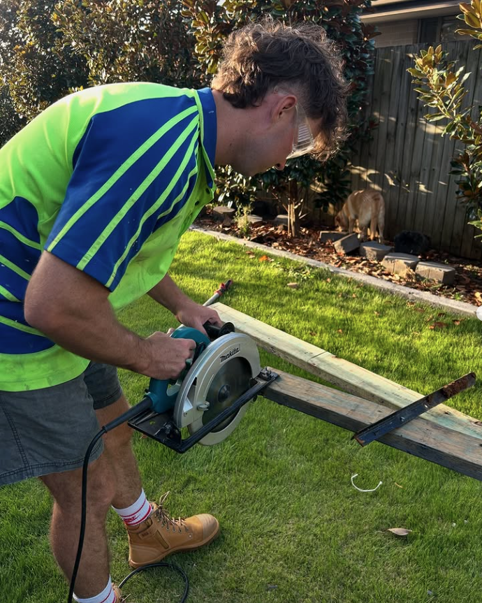 A tradie using a circular saw to cut timber outdoors on a residential job site
