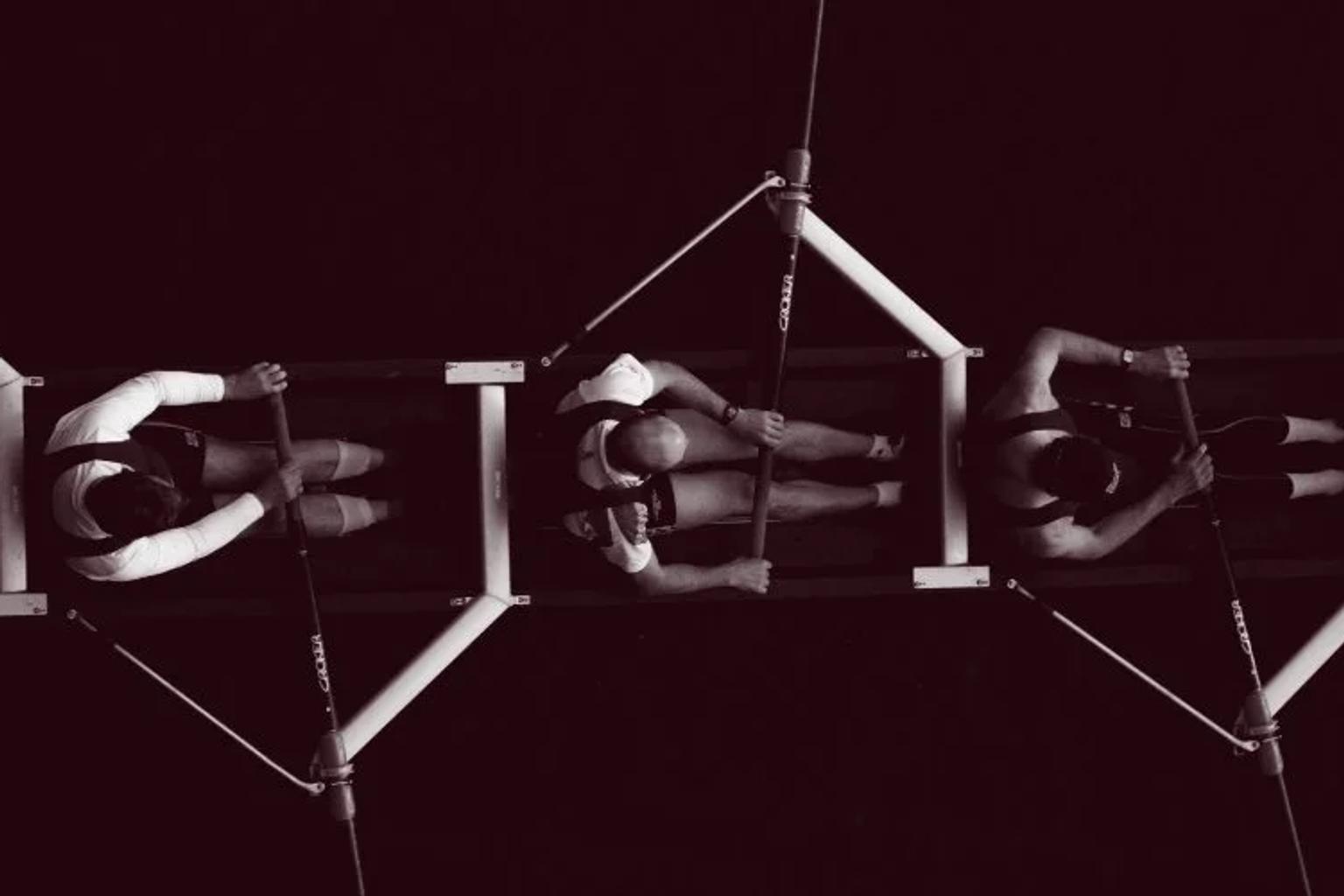 Five men rowing a boat together, representing coordinated teams working toward a shared goal