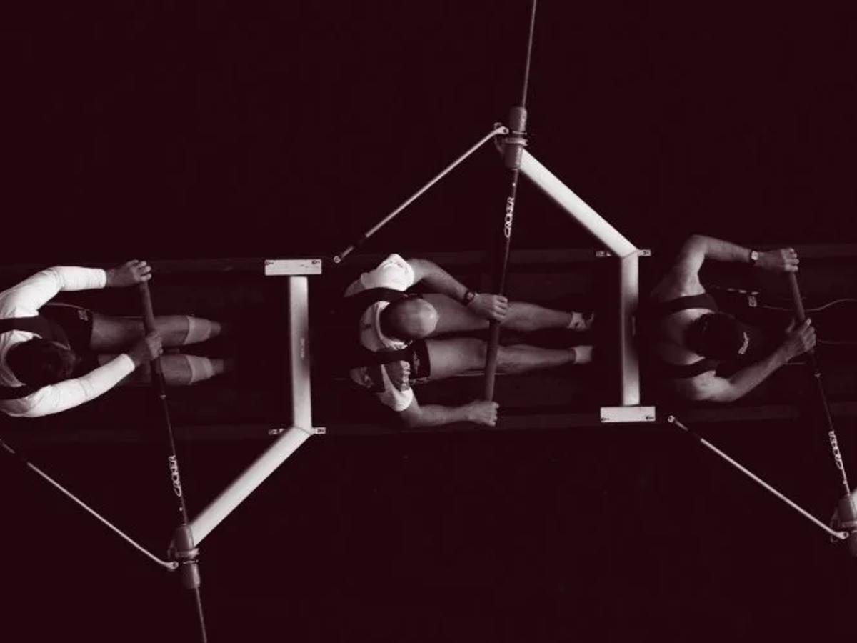 Five men rowing a boat together, representing coordinated teams working toward a shared goal