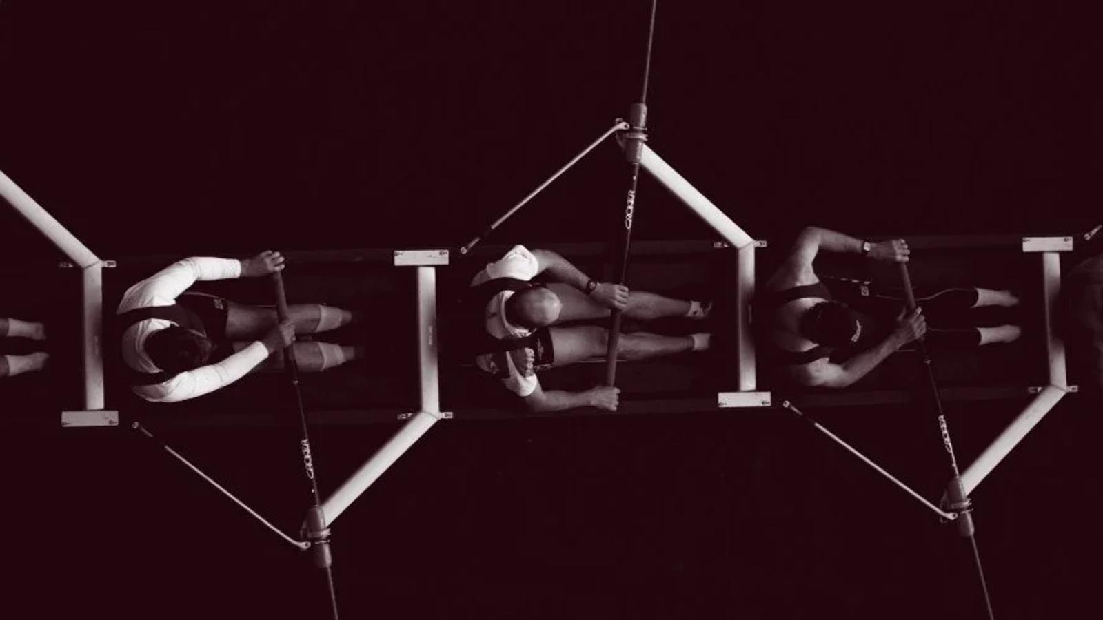 Five men rowing a boat together, representing coordinated teams working toward a shared goal