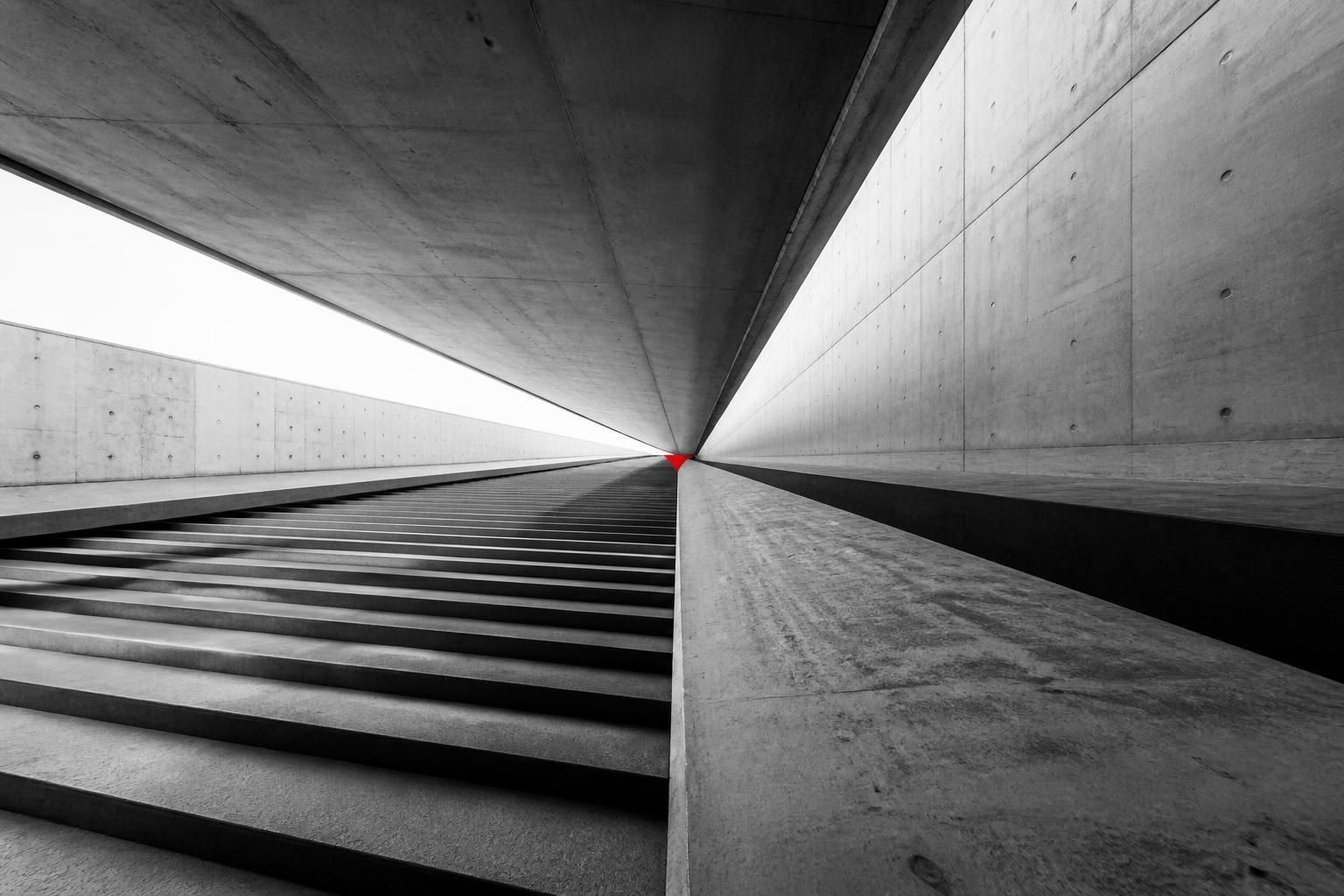 Converging concrete lines and steps meeting at a single vanishing point, with a small accent mark at the convergence.
