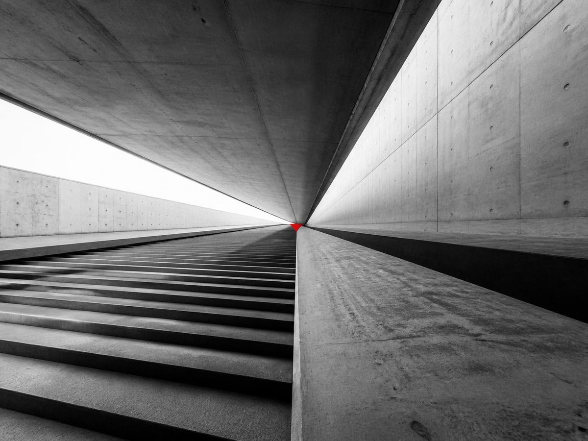 Converging concrete lines and steps meeting at a single vanishing point, with a small accent mark at the convergence.