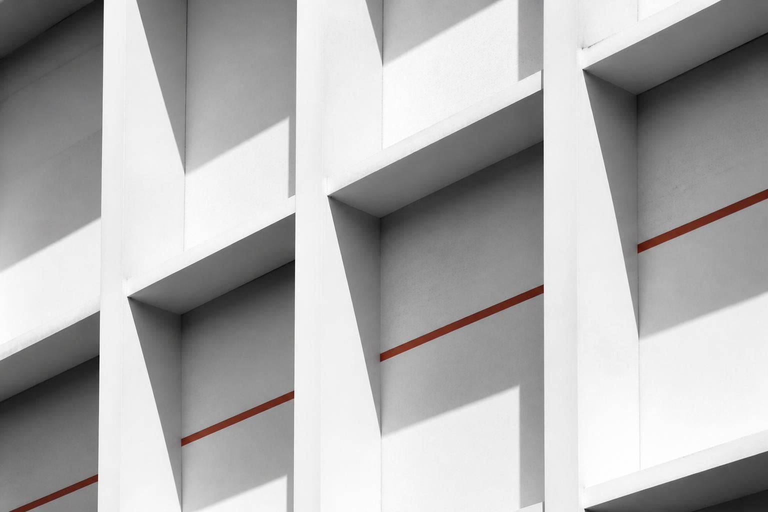 White concrete facade with a rigid repeating structural grid and hard shadows, crossed by a single accent line.