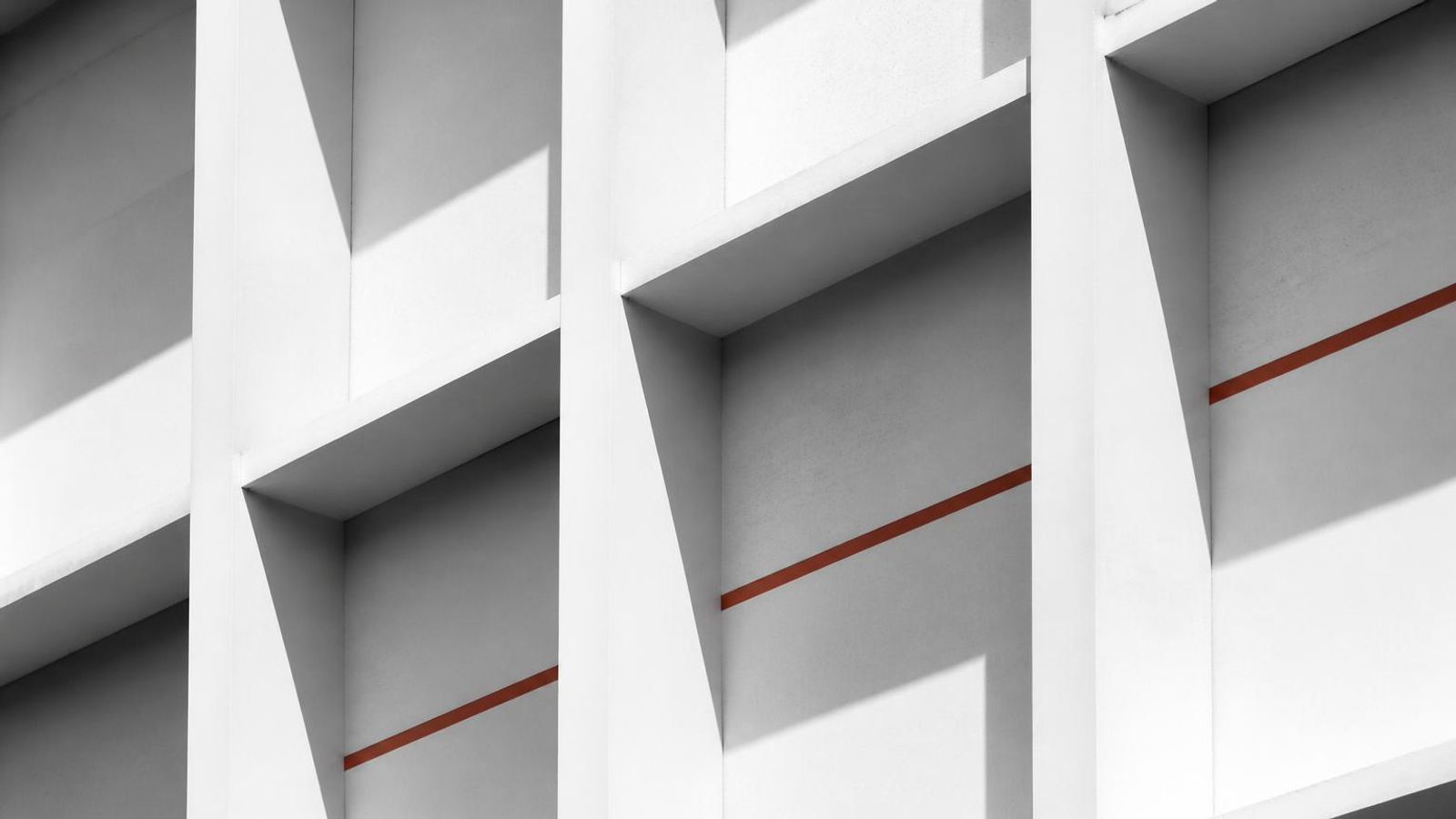 White concrete facade with a rigid repeating structural grid and hard shadows, crossed by a single accent line.