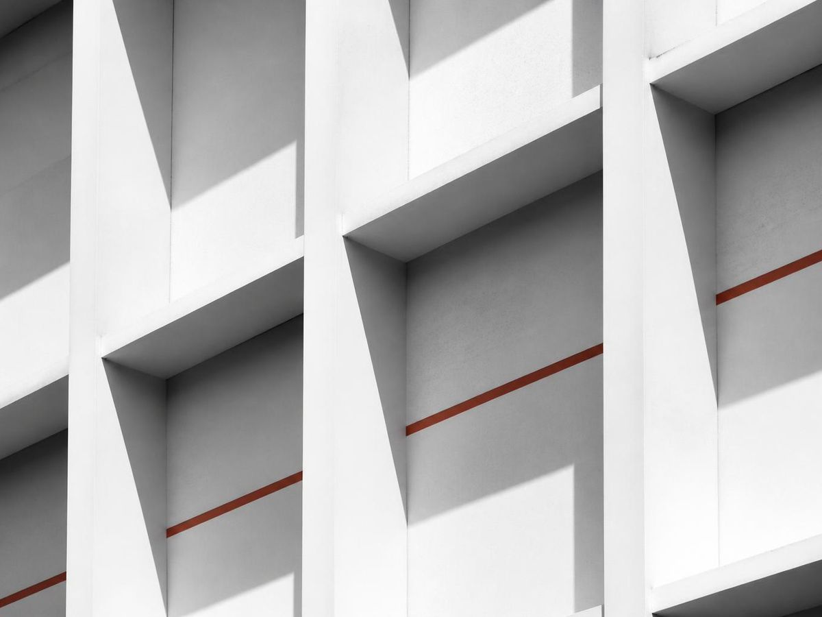 White concrete facade with a rigid repeating structural grid and hard shadows, crossed by a single accent line.