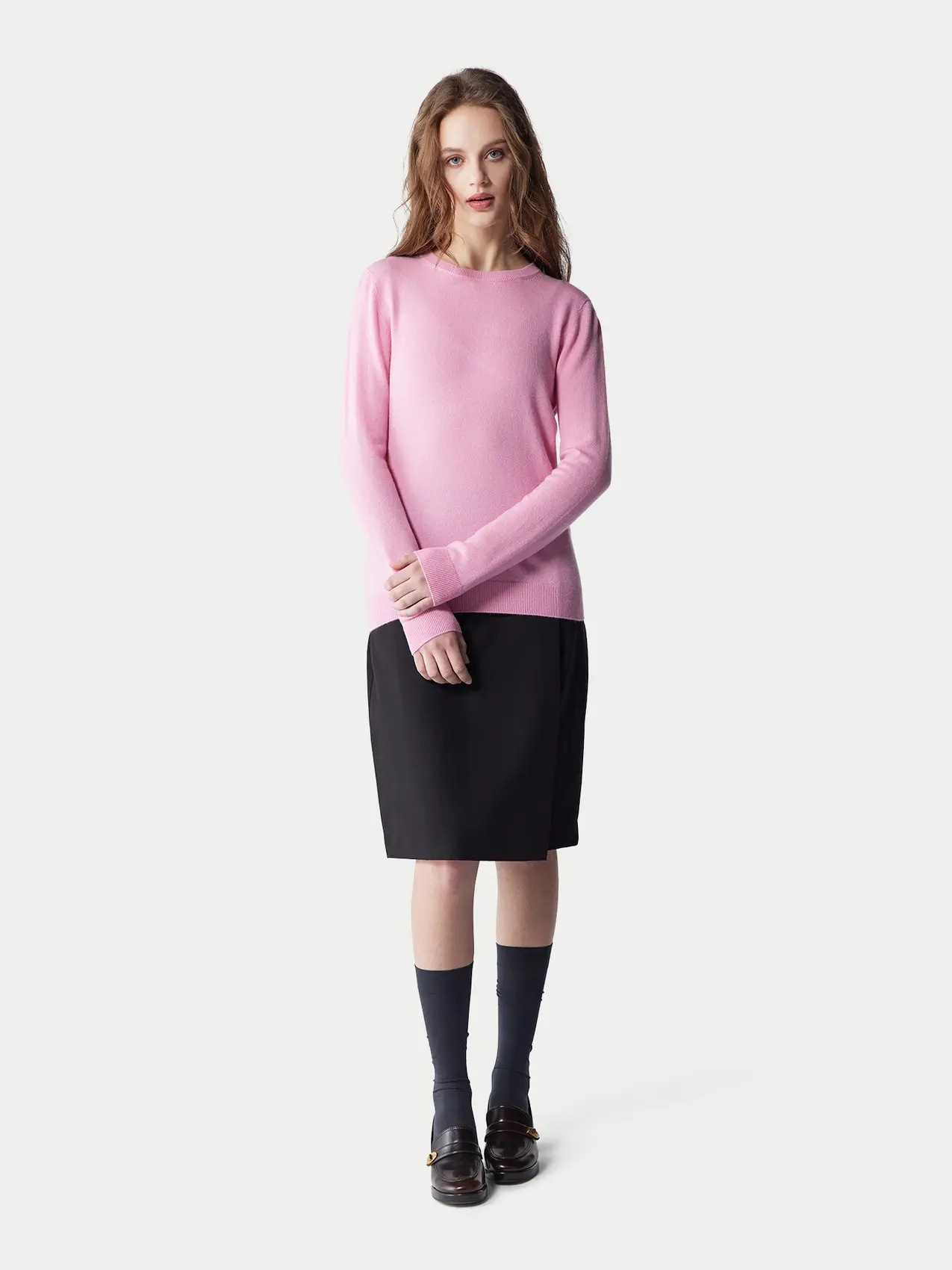 Women's office look with baby pink cashmere crewneck sweater, black midi skirt and black loafers