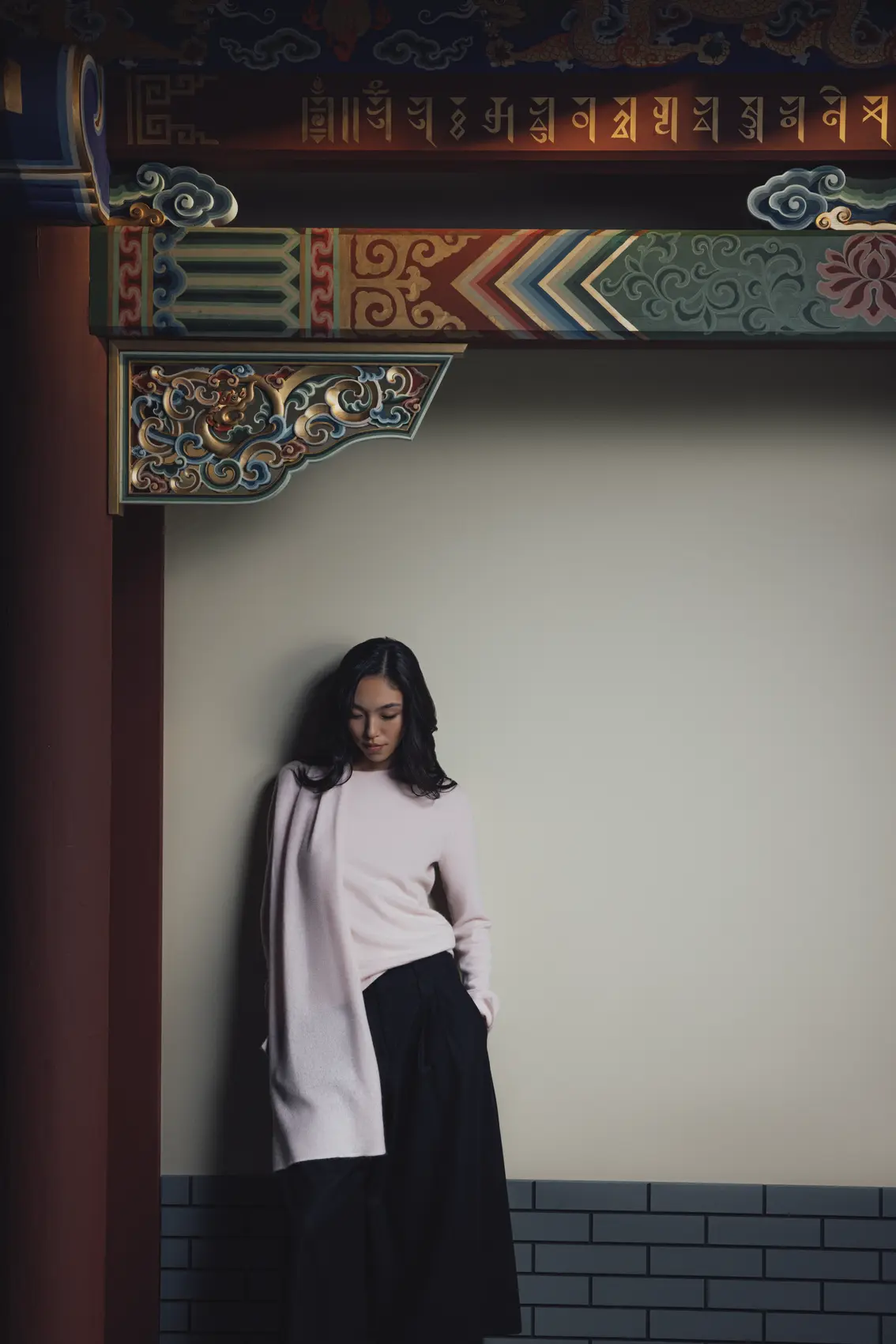 Woman in a soft pink cashmere sweater leaning against a wall beneath ornate architectural details | GOBI Cashmere