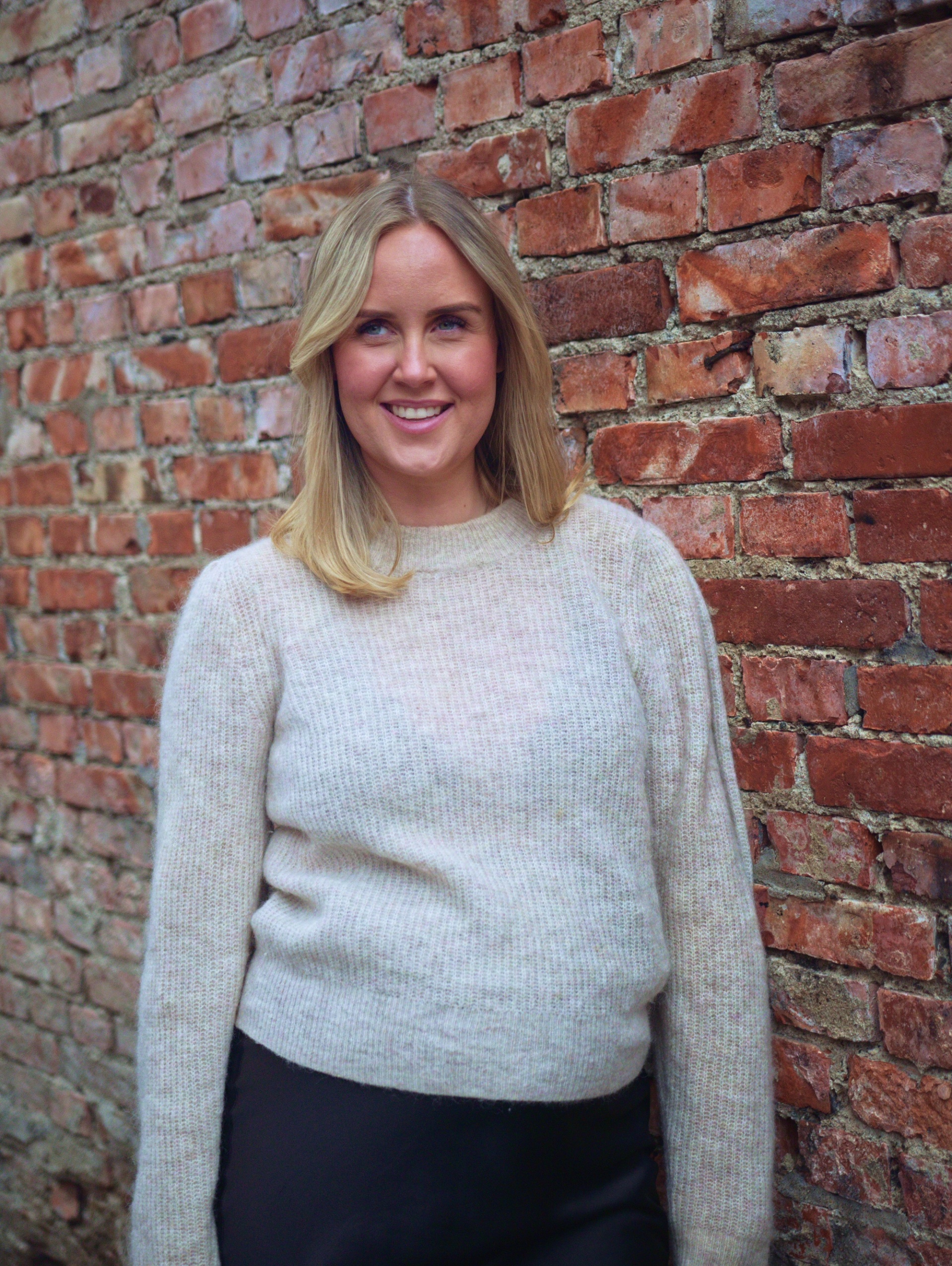 Kvinna som står lutad mot en tegelvägg och ler