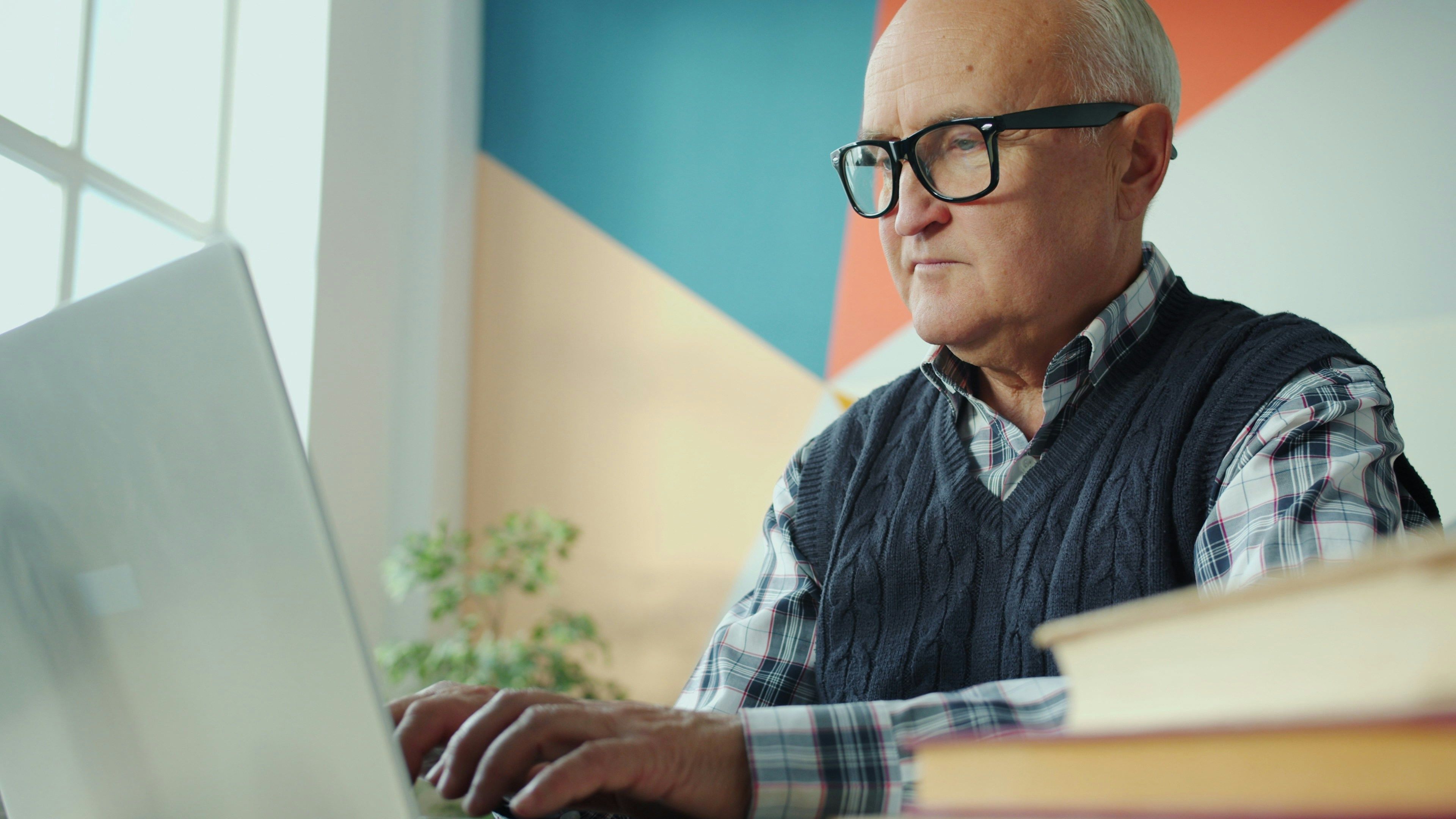 An older man wearing glasses, typing on a laptop