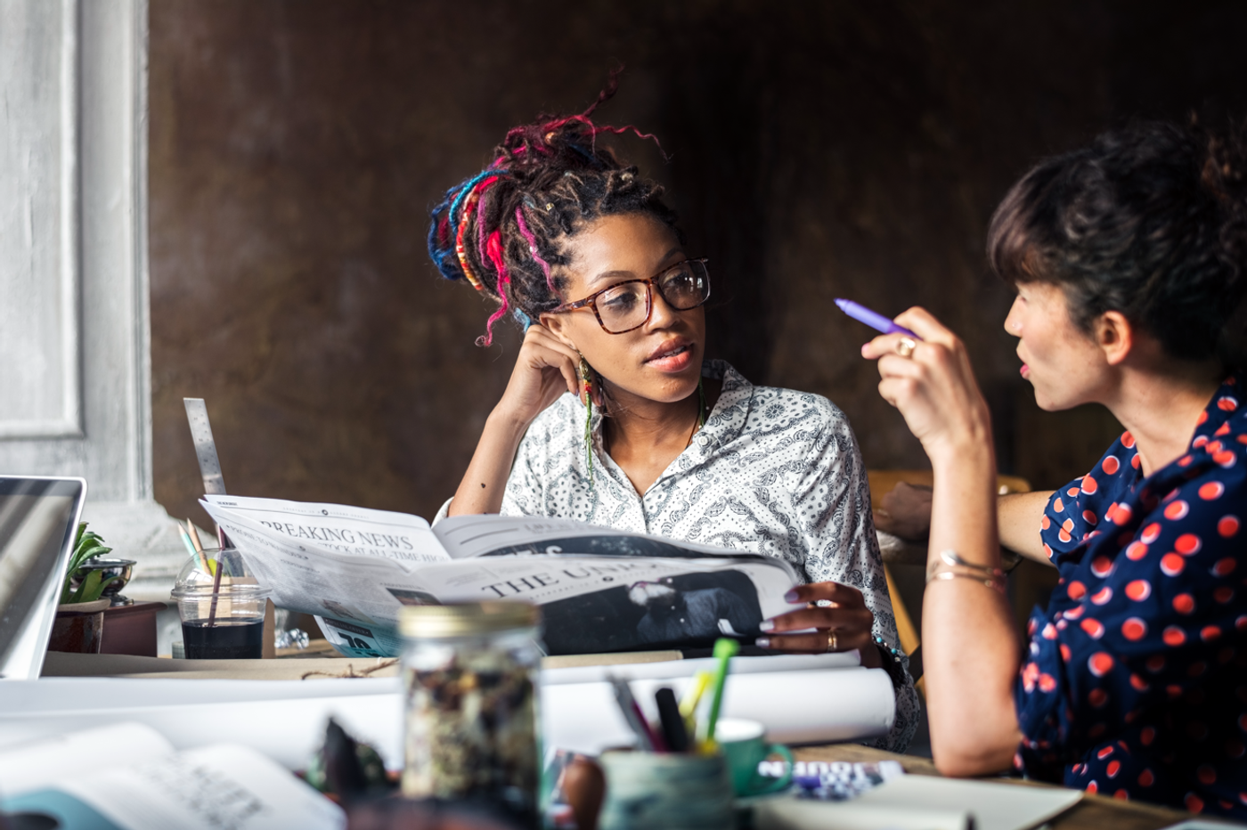 Candid stock photo of two women talking at a table with a newspaper