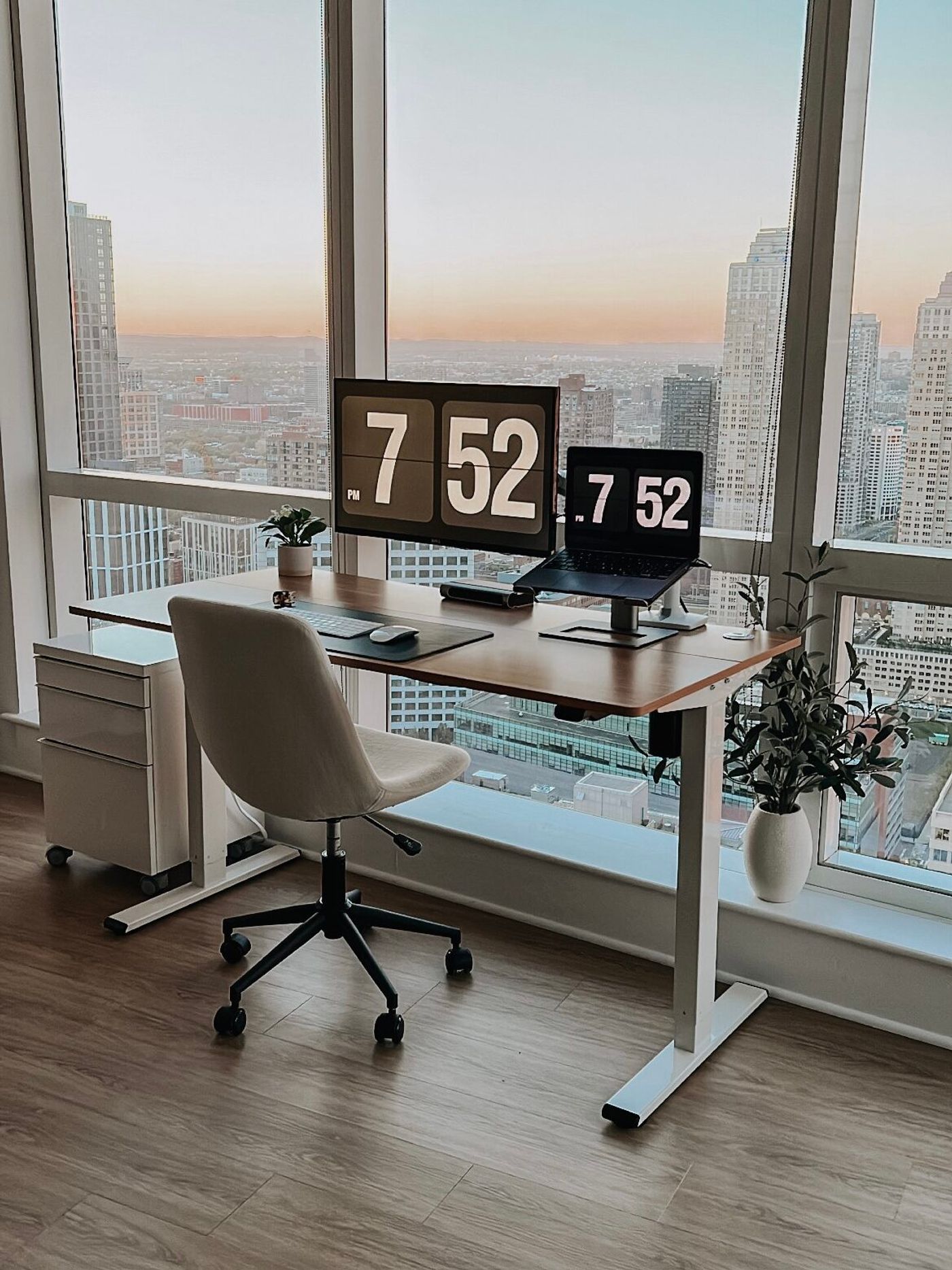Katie Eckstrom's home office desk with a flip clock, monitor and city view