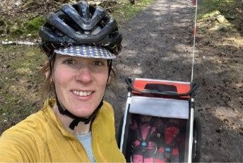 Hetty in a cycling helmet, with a bike trailer on the trail behind her