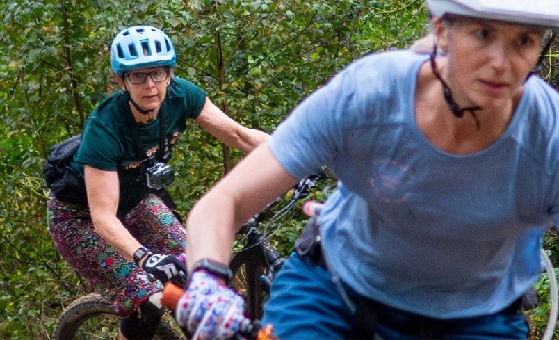 Two women riding mountain bikes along a wooded trail