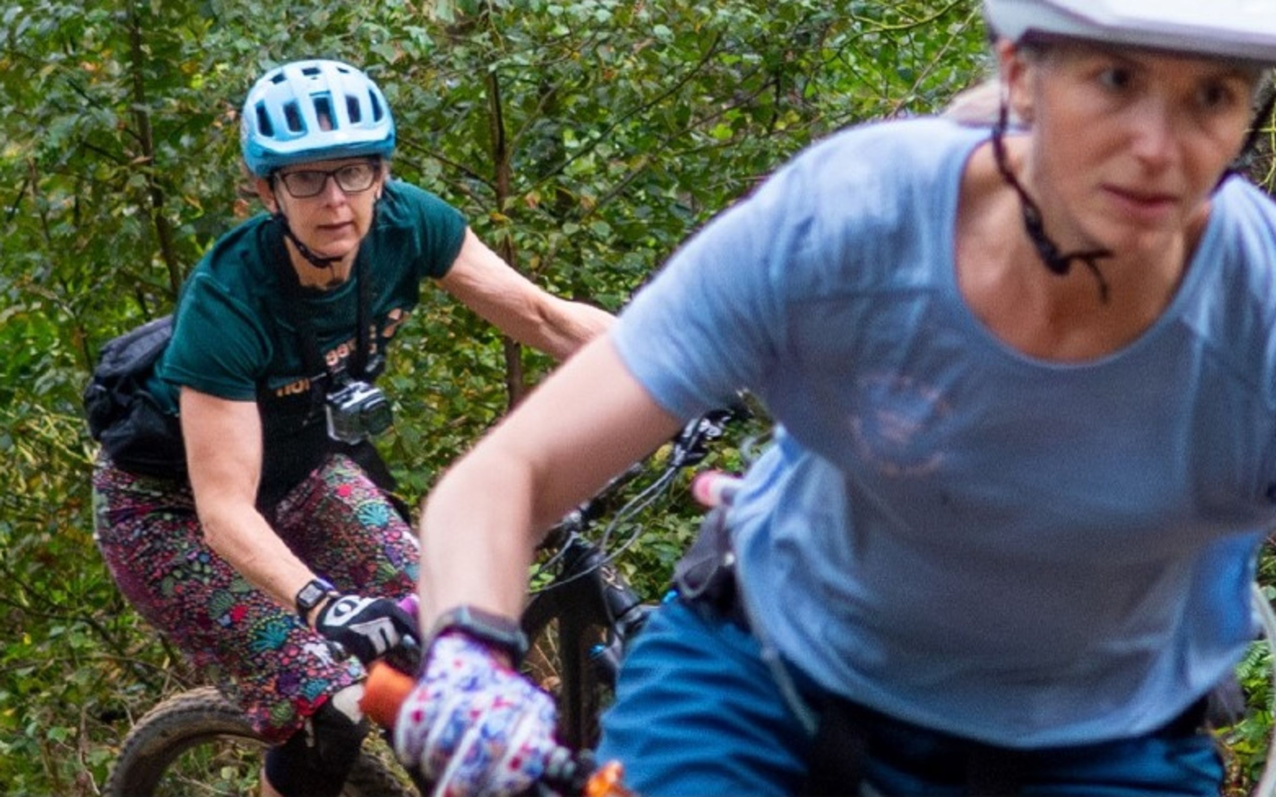 Two women riding mountain bikes along a wooded trail