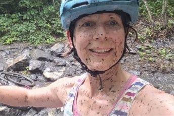 Fiona, smiling and splattered with mud, wearing a cycling helmet