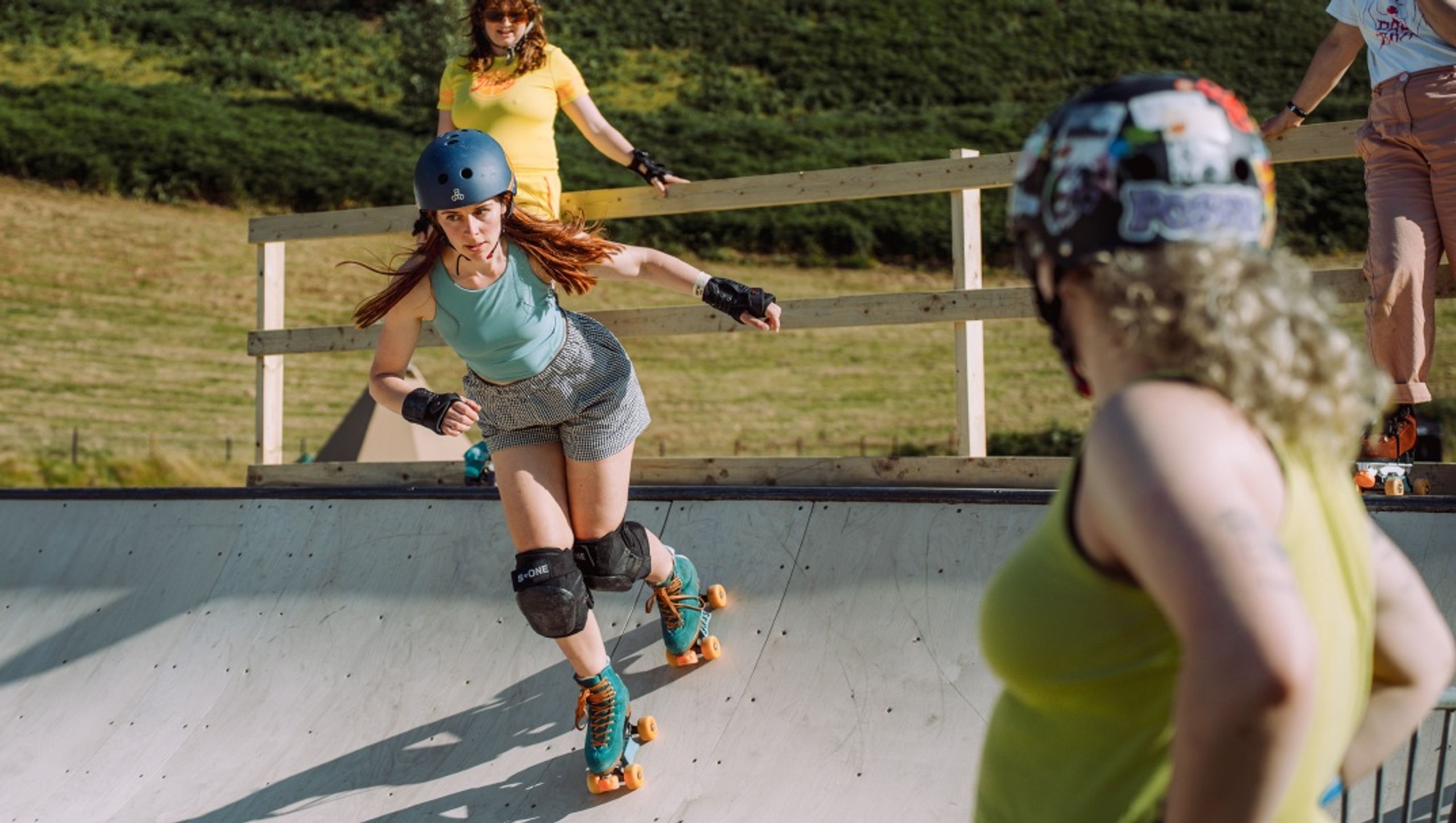 A roller skater dropping into a wooden ramp while other skaters watch from the deck