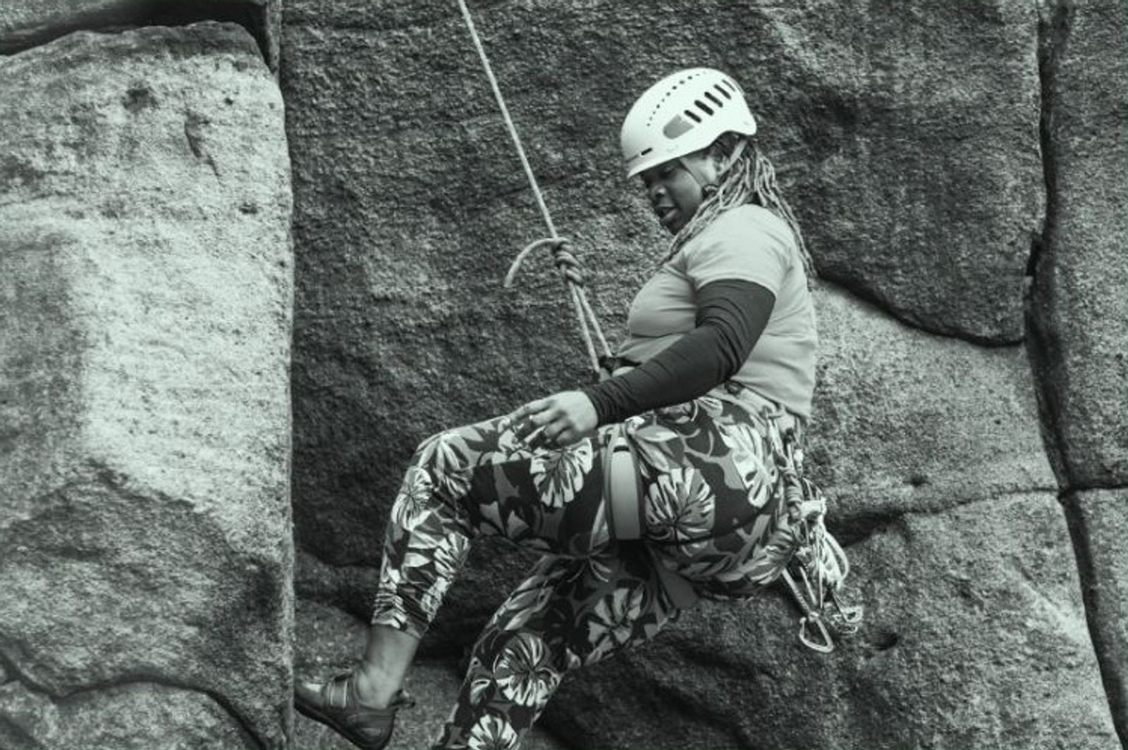 A woman in a helmet abseiling down a gritstone rock face