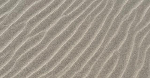 Fine wind-shaped lines create uneven ripples across pale desert sand.